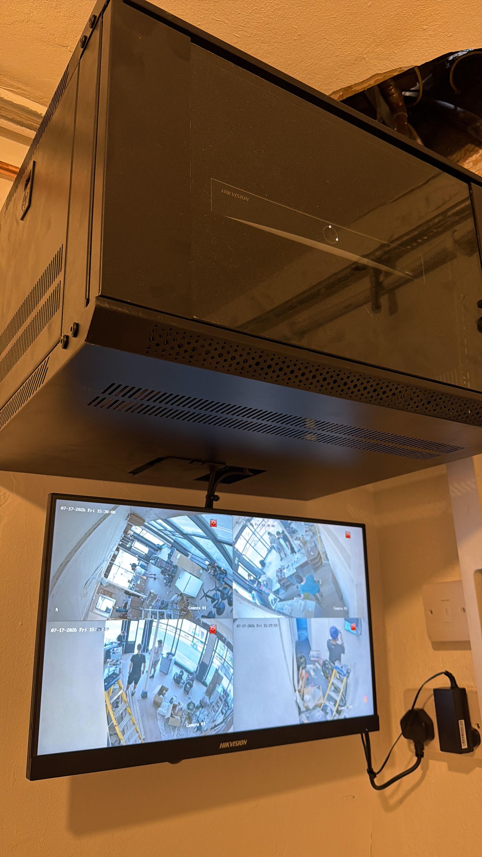 Hikvision CCTV recorder and monitor installed above shop counter showing four camera feeds, Bristol